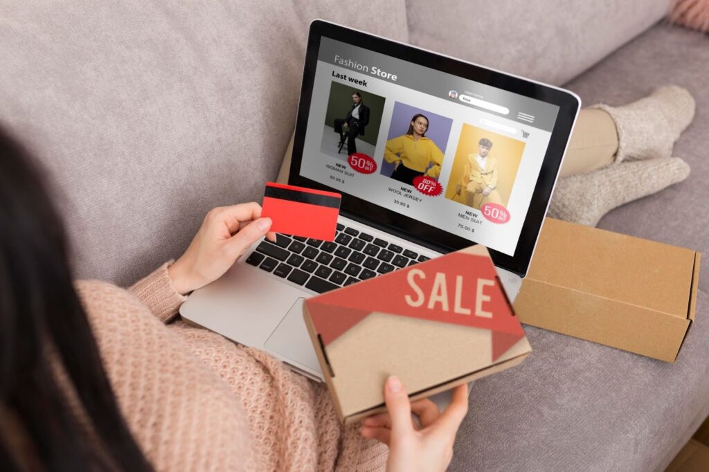 Woman shopping online from home using a credit card and laptop, browsing discounted fashion deals on an ecommerce website — concept of online clothing sales, holiday discounts, digital retail experience, and ecommerce shopping behavior in 2025.