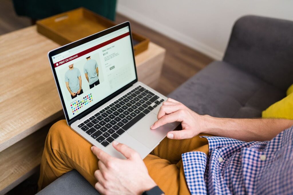 Man shopping for custom t-shirts on a print-on-demand ecommerce website using a laptop, showing streamlined product pages and optimized site navigation UX.