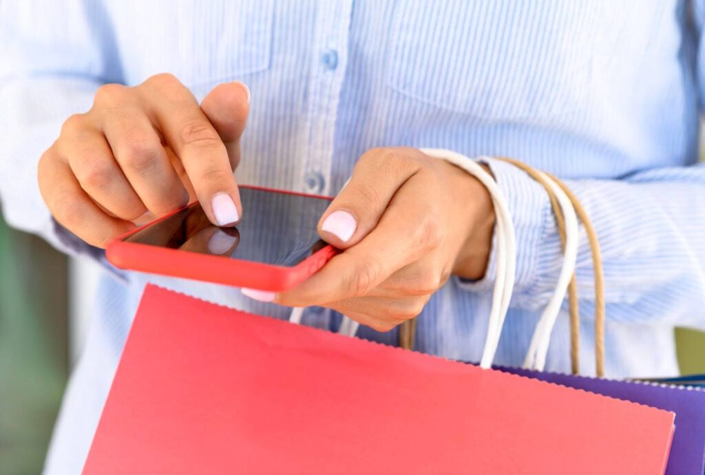 Close-up of a woman holding a smartphone and shopping bags, indicating mobile shopping and interaction with the best free apps on Shopify for e-commerce.