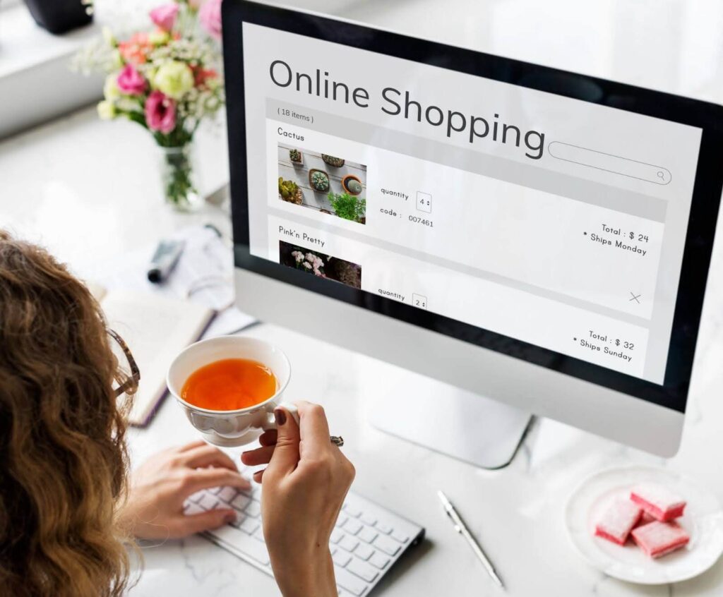 Woman drinking tea while viewing an online shopping site on a desktop, showcasing the user-friendly interface made possible by building themes and optimizing Shopify performance.