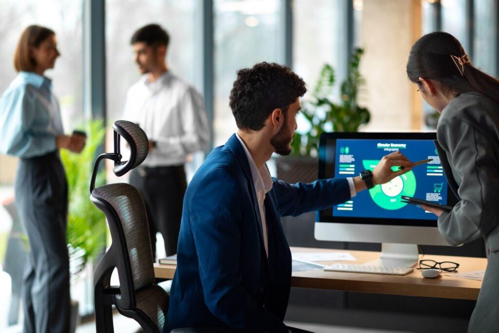 Colleagues discussing business analytics displayed on a desktop screen, utilizing cloud-based productivity suites to enhance productivity software performance.